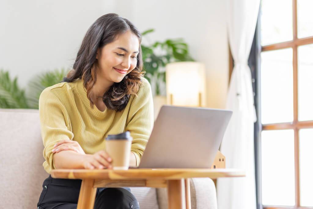 Eine junge Frau sitzt lächelnd am Laptop in einem hell erleuchteten Raum